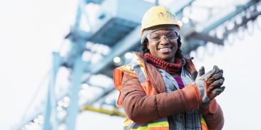 Woman wearing a hard hat, safety vest and safety goggles, working at a shipping port.